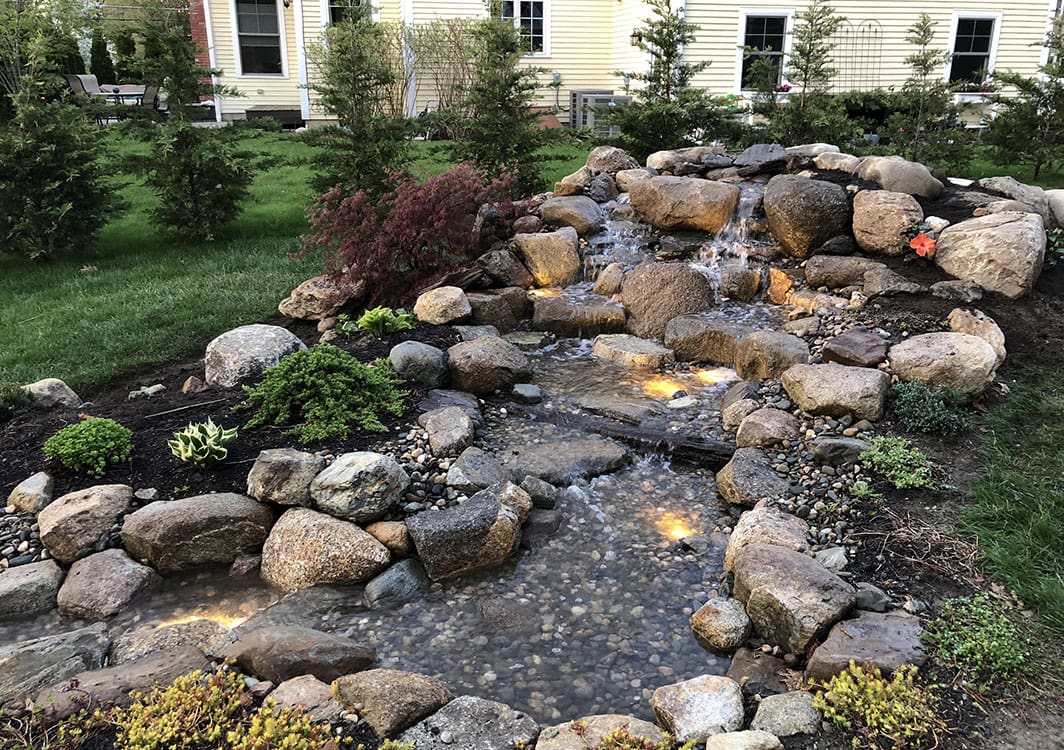 Pondless water feature framed by evergreen shrubs
