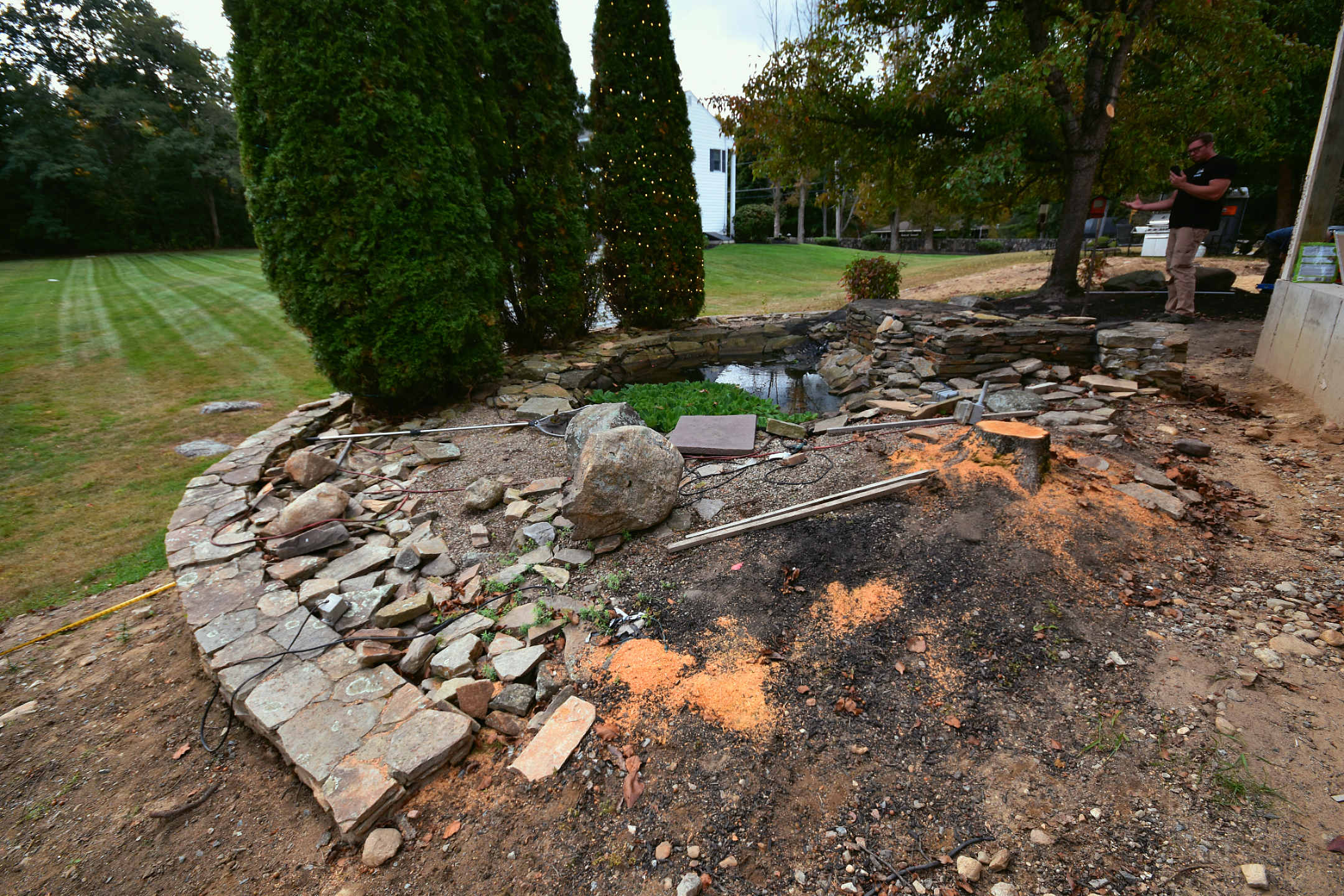 Stone landscape under construction with pond and trees.